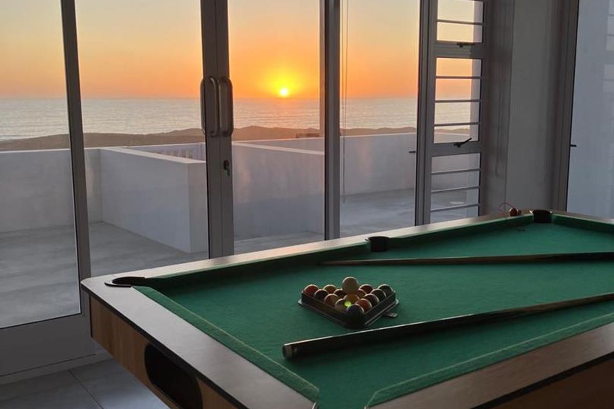Spacious living area featuring large glass sliding doors that open to a balcony with stunning sunset ocean views.