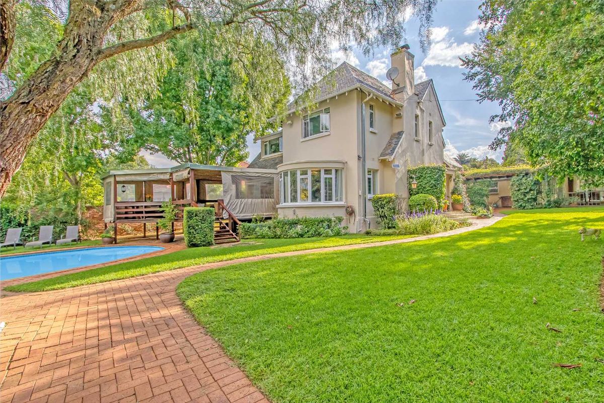 A view of the rear exterior of the house, featuring a swimming pool, a raised wooden deck, and a well-maintained garden.