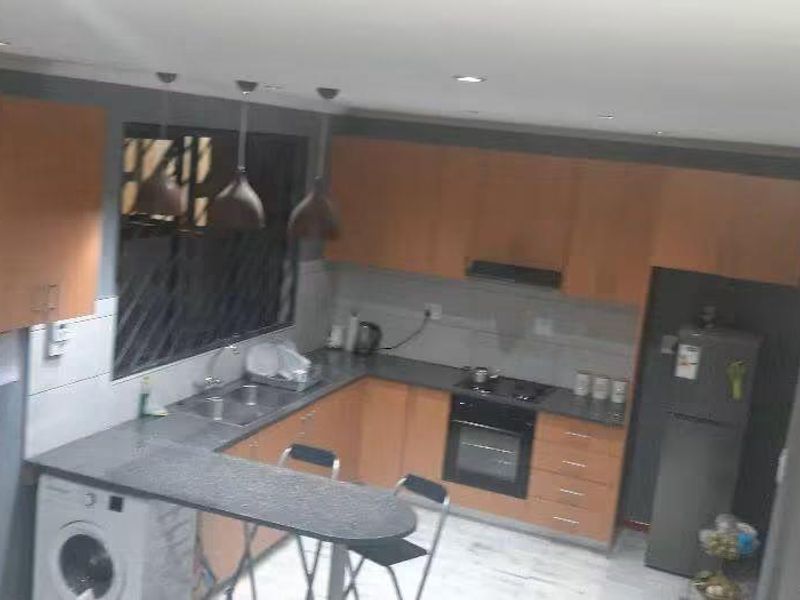 A functional kitchen featuring wooden cabinetry, dark countertops, integrated appliances, and a breakfast bar, with some areas requiring minor finishing touches.