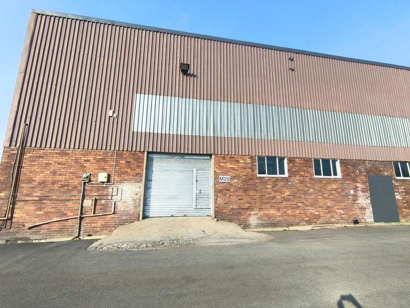 Industrial warehouse exterior featuring a brick and corrugated metal facade, a roller shutter door, and a concrete loading ramp.