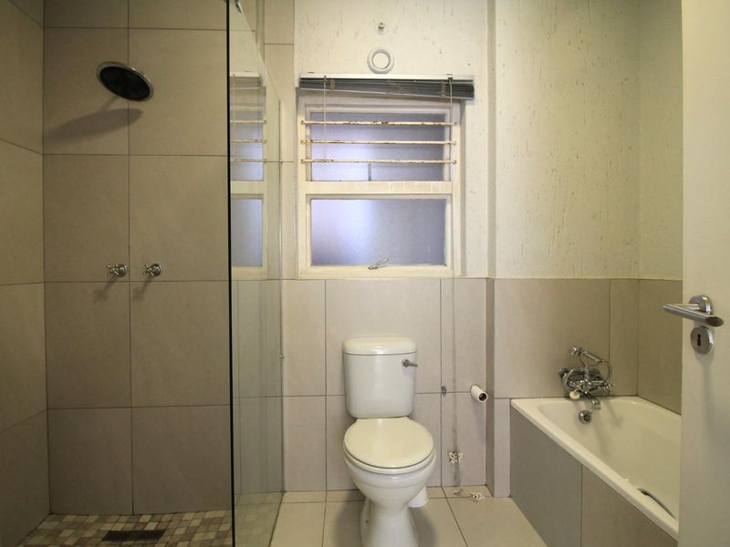 A functional bathroom featuring a combined shower and bathtub, tiled finishes, and a toilet. The space requires cosmetic updates to improve its overall condition.