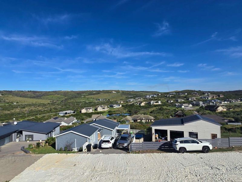 An elevated aerial view of a residential neighborhood featuring modern homes with metal roofs and solar panel installations under a clear blue sky.
