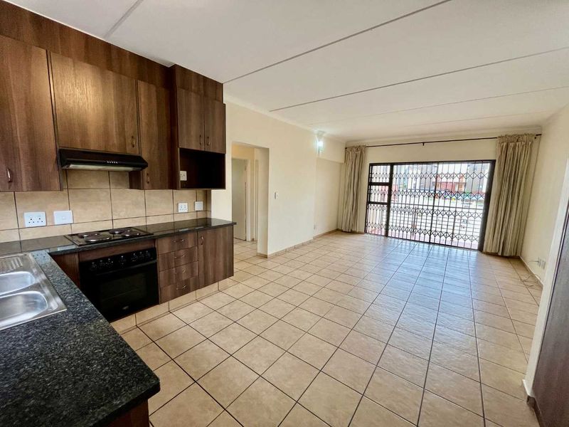 Open-plan living area featuring a functional kitchen with dark wood cabinetry, granite countertops, and tiled flooring, leading to a secure sliding door entrance.