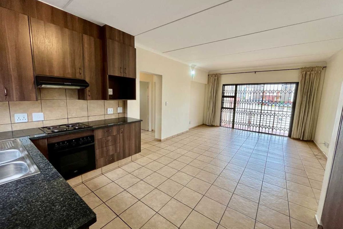 Open-plan living area featuring a functional kitchen with dark wood cabinetry, granite countertops, and tiled flooring, leading to a secure sliding door entrance.