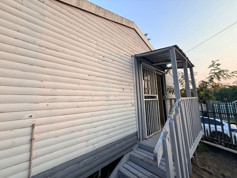 Exterior view of a cottage featuring timber cladding, a covered porch entrance with security gate, and wooden stairs.