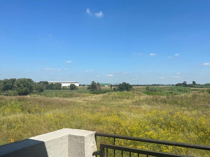 A view from a balcony overlooking an open field and natural landscape with a metal balustrade and concrete pillar in the foreground.