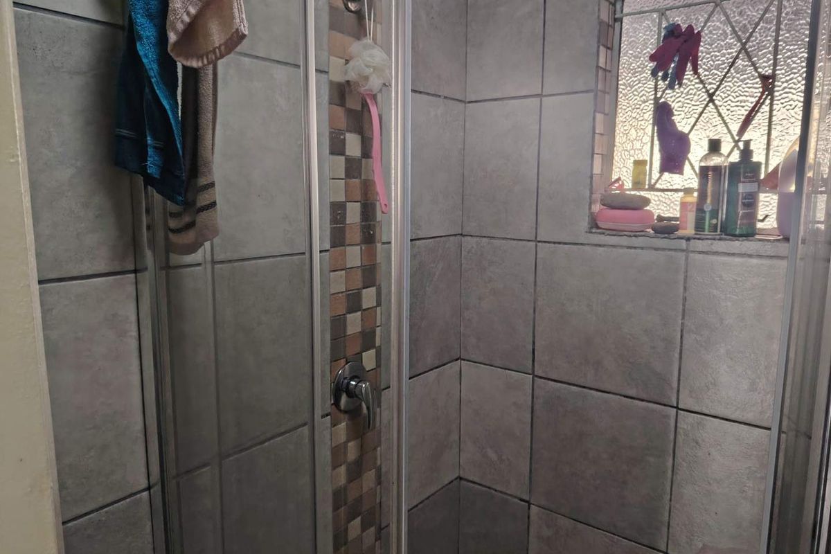 A compact shower enclosure featuring grey wall tiles with a decorative mosaic accent strip and a small frosted glass window.