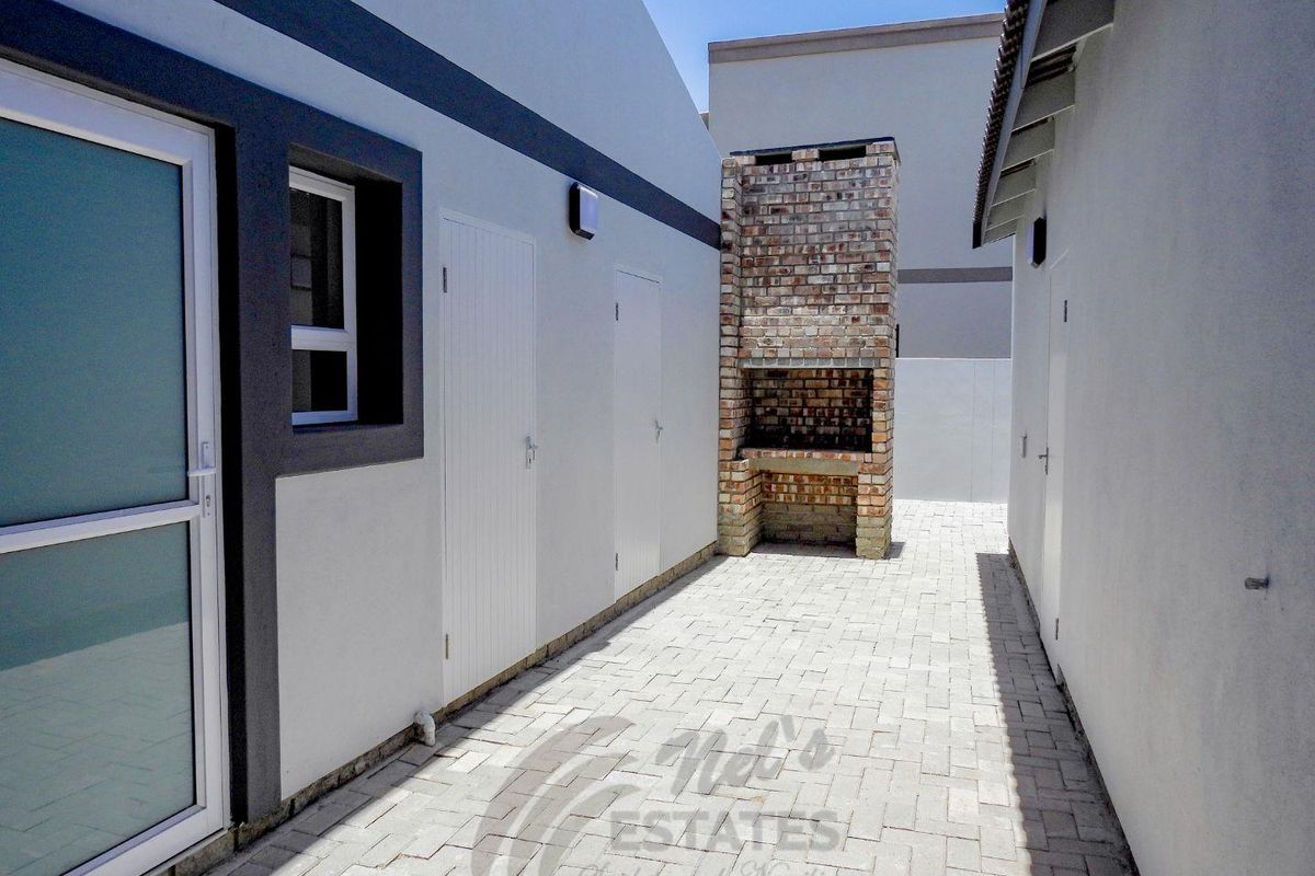 A paved outdoor courtyard area featuring a built-in brick braai or barbecue fireplace, accessible via multiple exterior doors.