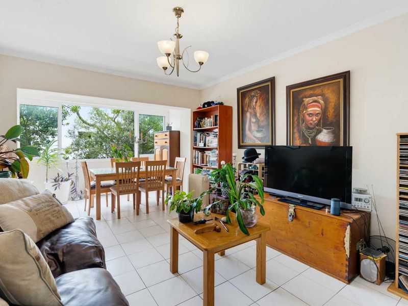 An open-plan living and dining area featuring tiled flooring, a large window providing natural light, and a central ceiling light fixture.