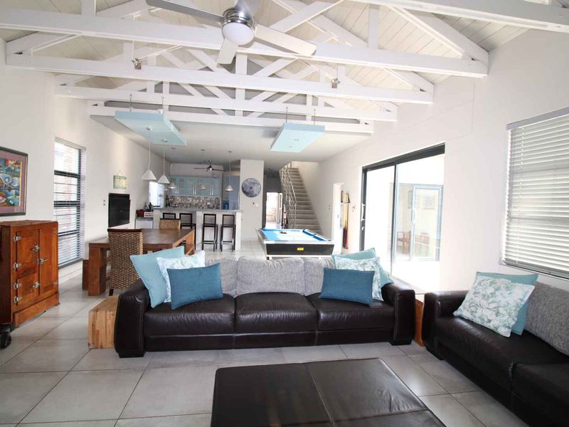 Spacious open-plan living area featuring high vaulted ceilings with exposed trusses, tiled floors, and seamless flow to the kitchen and dining space.