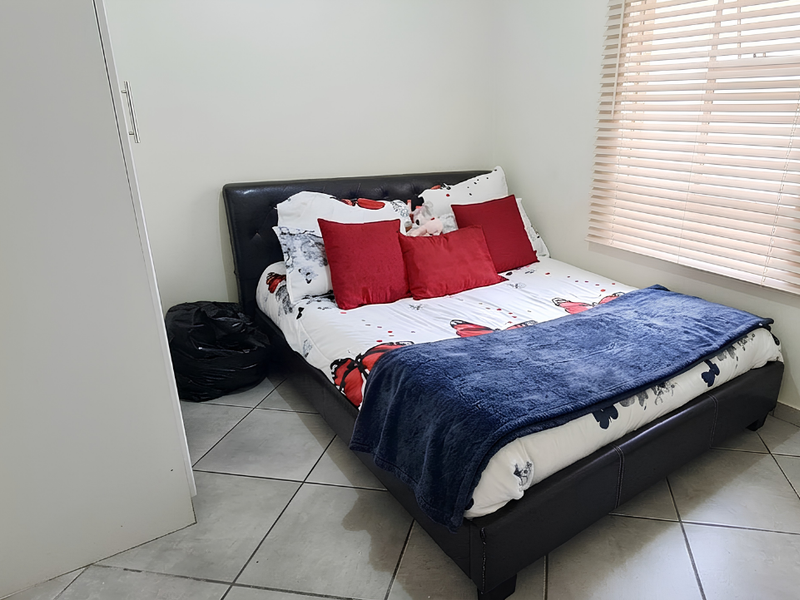 A well-maintained bedroom featuring neutral walls, tiled flooring, a built-in wardrobe, and venetian blinds for adjustable natural light.