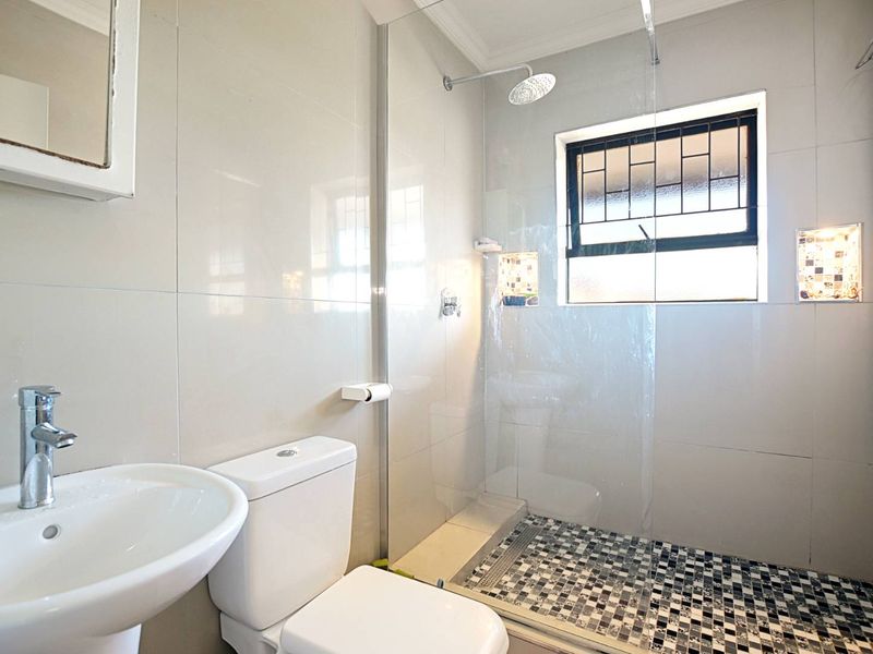 Modern bathroom featuring a pedestal basin, toilet, and a walk-in shower with a glass screen and decorative tiled floor.