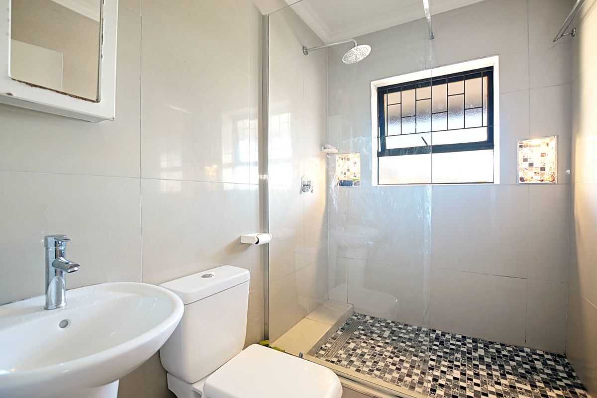 Modern bathroom featuring a pedestal basin, toilet, and a walk-in shower with a glass screen and decorative tiled floor.