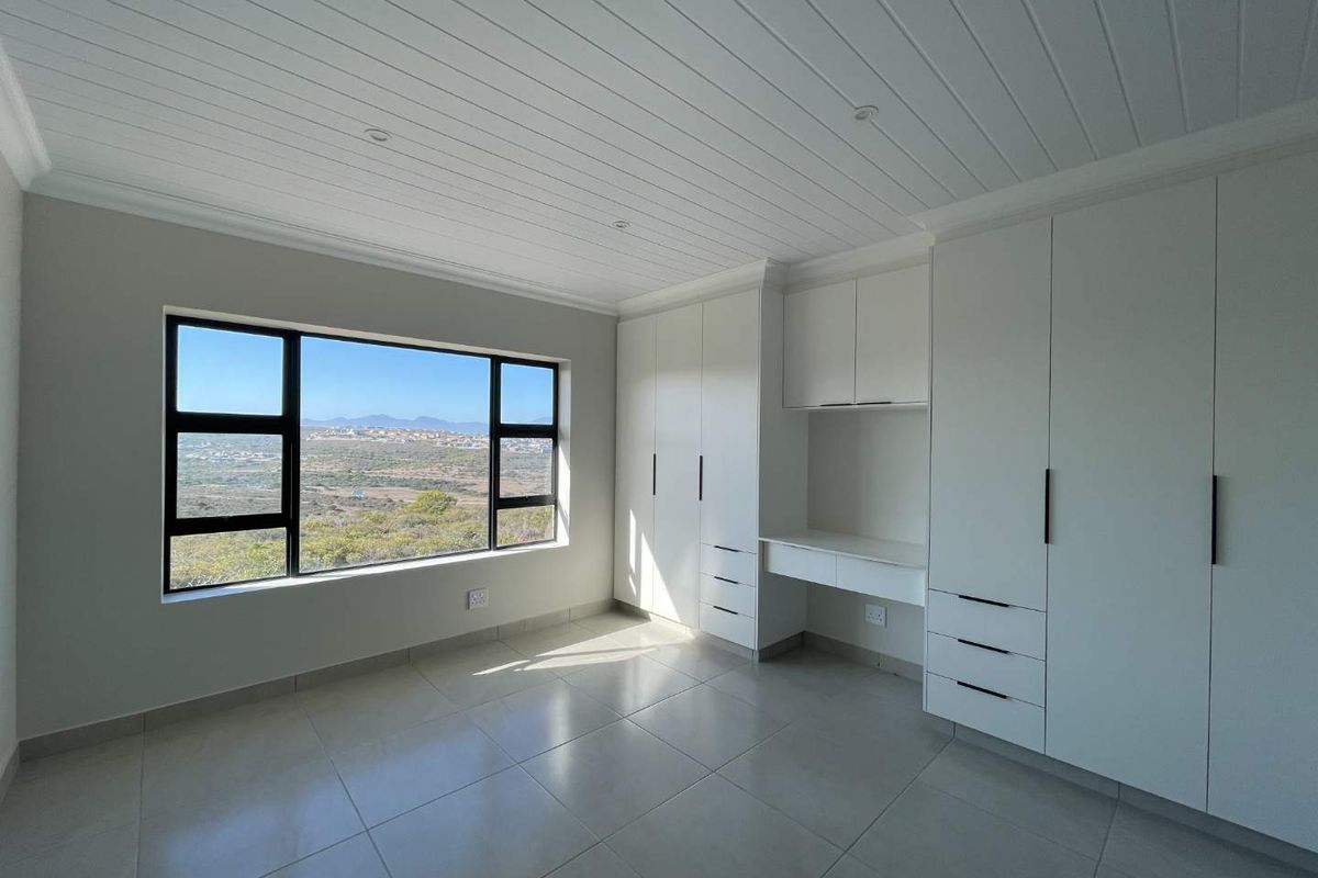 A bright, modern bedroom featuring built-in cabinetry with an integrated desk, tiled flooring, and large windows offering scenic landscape views.
