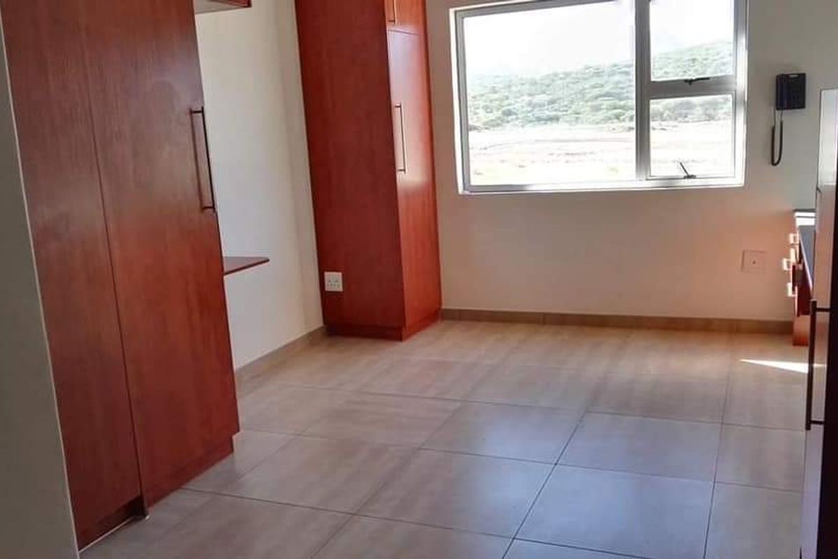 A functional bedroom or study area featuring built-in wooden cabinetry, tiled flooring, and a large window providing natural light and scenic views.