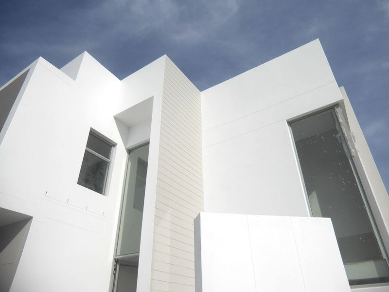 A modern architectural facade featuring clean white lines, large glass windows, and horizontal cladding elements, showcasing a contemporary residential design.