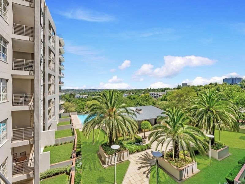 Elevated view overlooking the apartment complex grounds, featuring landscaped gardens, paved pathways, and a swimming pool area.