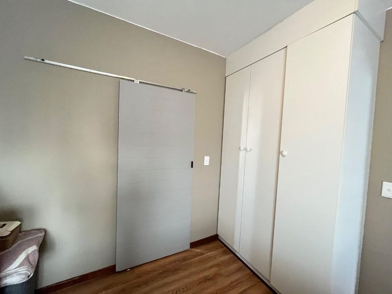 A clean bedroom featuring built-in cupboards, a modern sliding barn door, and durable laminate flooring.