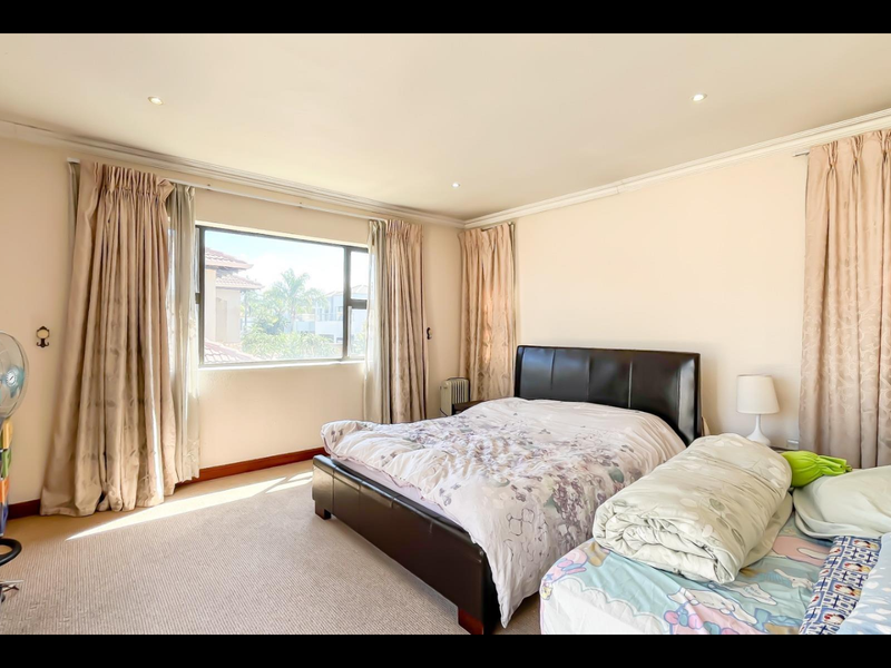 A spacious bedroom featuring neutral walls, carpeted flooring, recessed downlighting, and large windows with curtain rails.