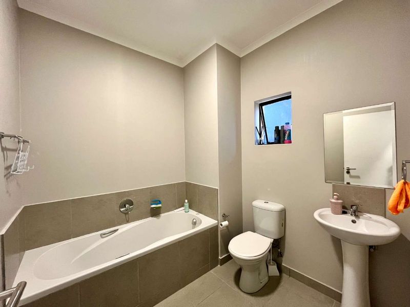 A clean and functional bathroom featuring a built-in bathtub, pedestal sink, toilet, and neutral wall and floor tiling.