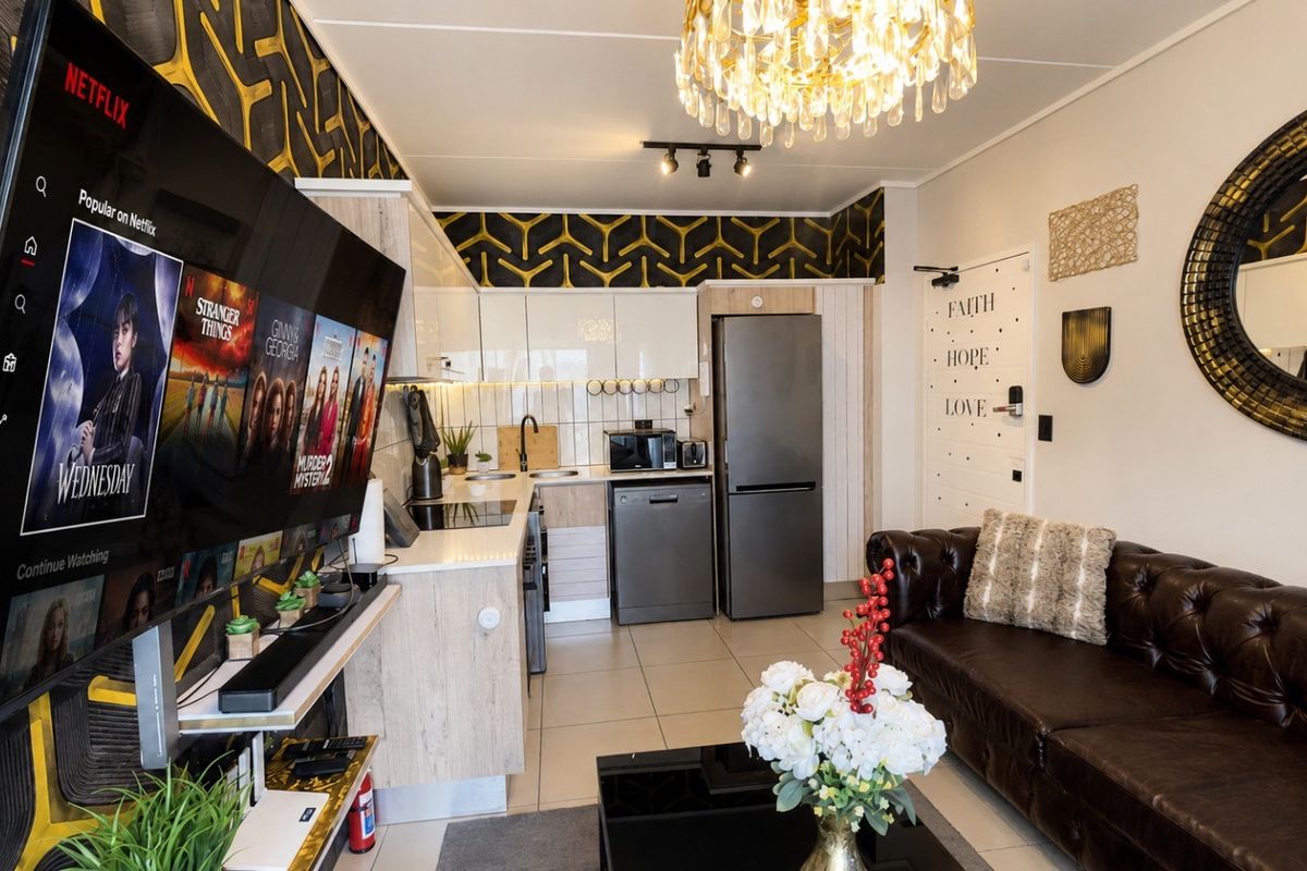 Modern open-plan living area featuring a compact kitchen with built-in cabinetry, integrated appliances, and tiled flooring, seamlessly connected to the lounge space.