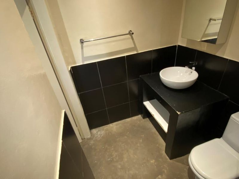A compact bathroom featuring a vessel sink on a built-in vanity, a toilet, and black tiled splashbacks.