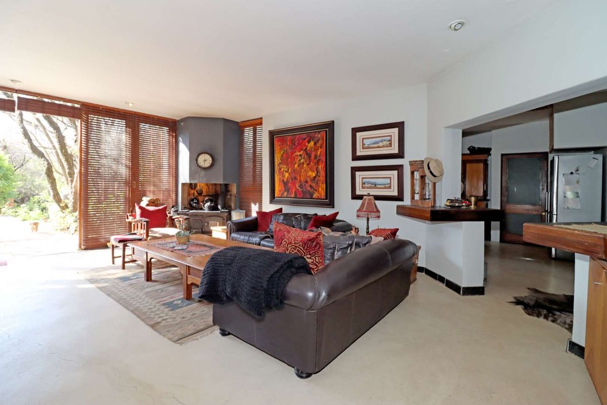Spacious living room featuring polished concrete floors, a built-in fireplace, and large windows with timber blinds, offering a seamless flow to the adjacent kitchen area.