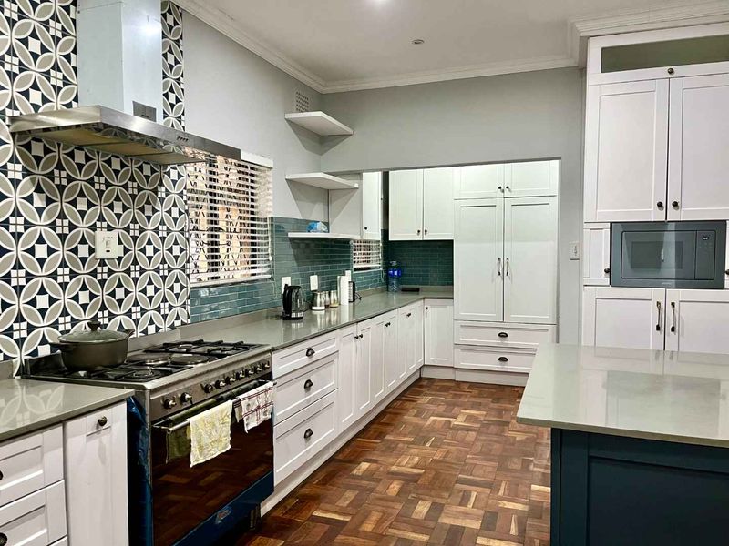 Modern kitchen featuring white shaker cabinetry, stone countertops, gas stove with extractor, and a striking patterned tile backsplash over parquet flooring.