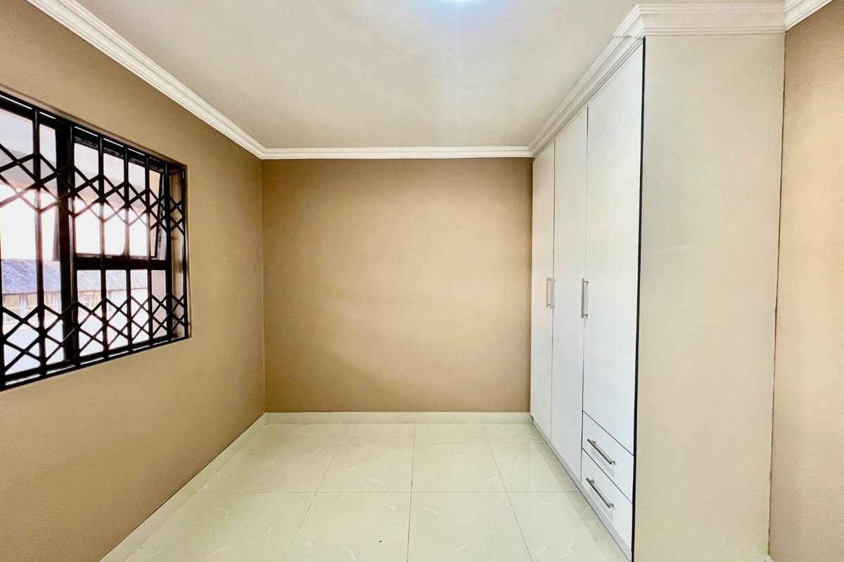 A clean, empty bedroom featuring neutral wall tones, tiled flooring, and a large built-in wardrobe with integrated drawers.