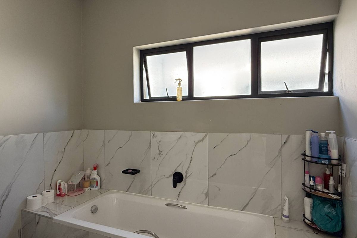 A modern bathroom featuring a built-in bathtub with marble-look wall tiling, black matte fixtures, and a horizontal window for natural light.