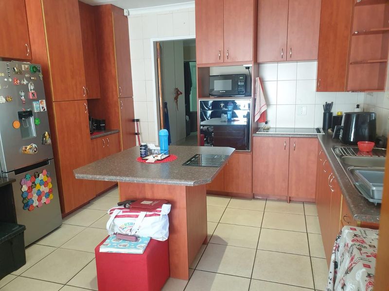 A functional kitchen featuring wood-look cabinetry, laminate countertops, built-in oven, microwave, and tiled flooring, offering a practical layout for daily meal preparation.