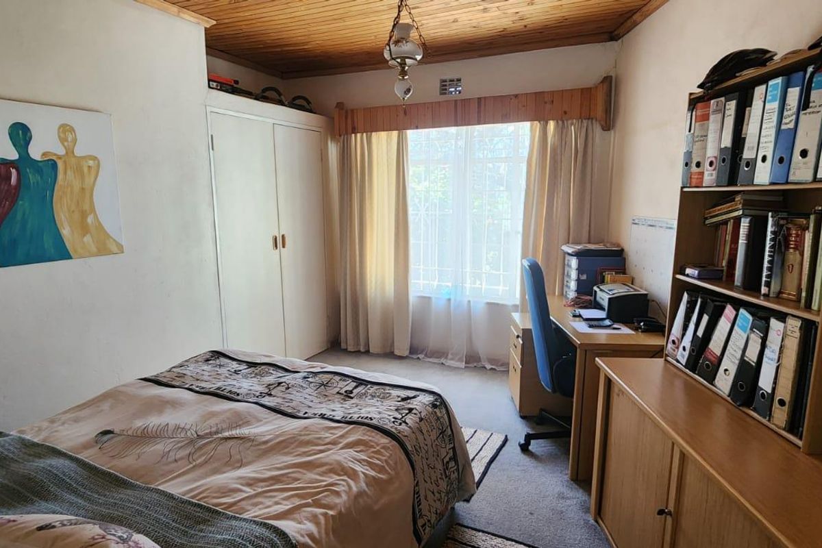 A functional bedroom featuring built-in cupboards, a timber-clad ceiling, and a window with security bars, providing a practical living space.