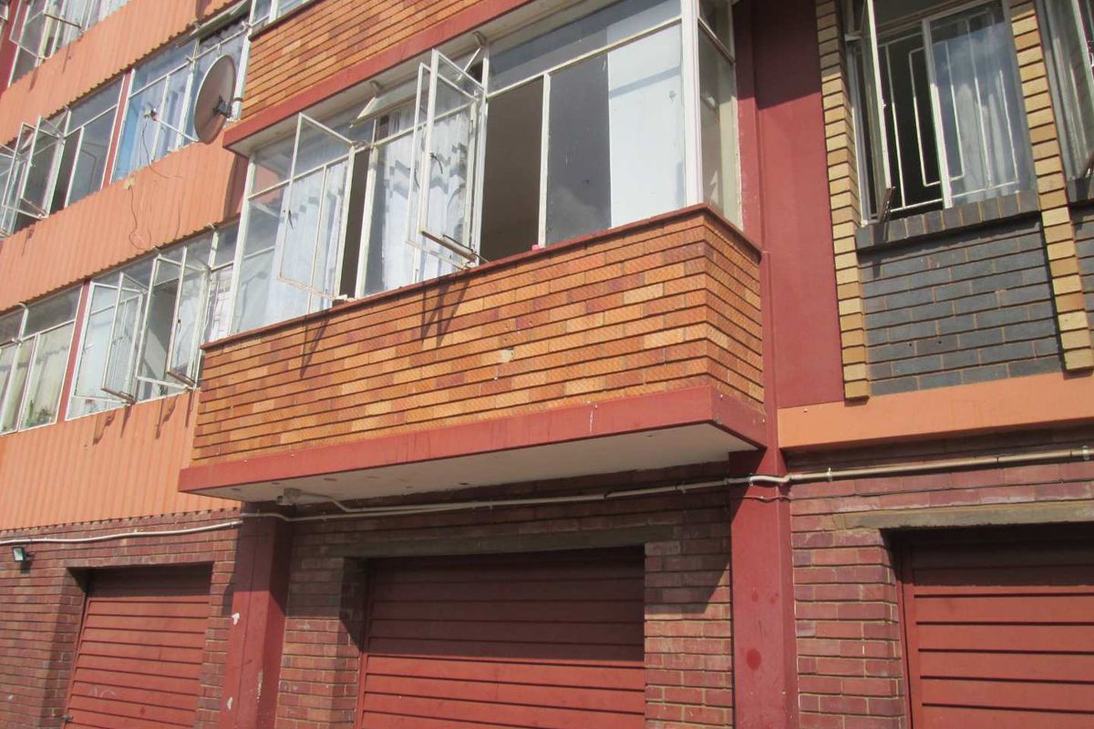 Exterior view of an apartment building facade featuring brick construction, enclosed balcony area, and ground-level garage access.