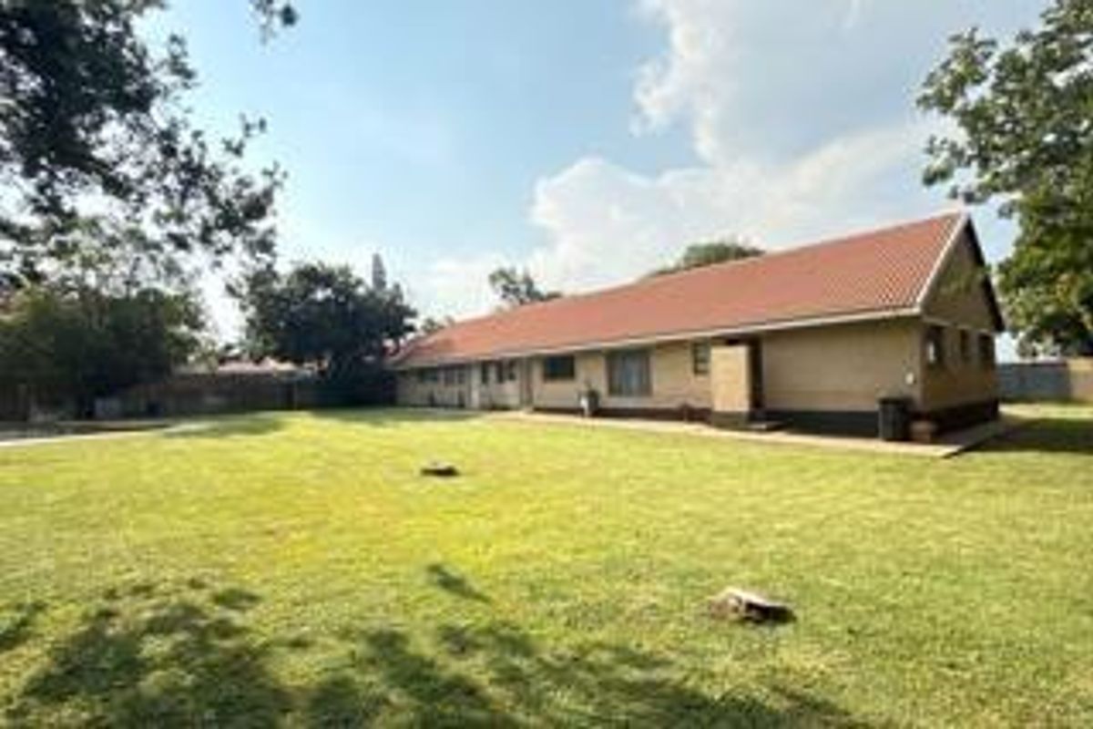 A view of the rear exterior of the house, featuring a large, open lawn area and a single-story building with a tiled roof.