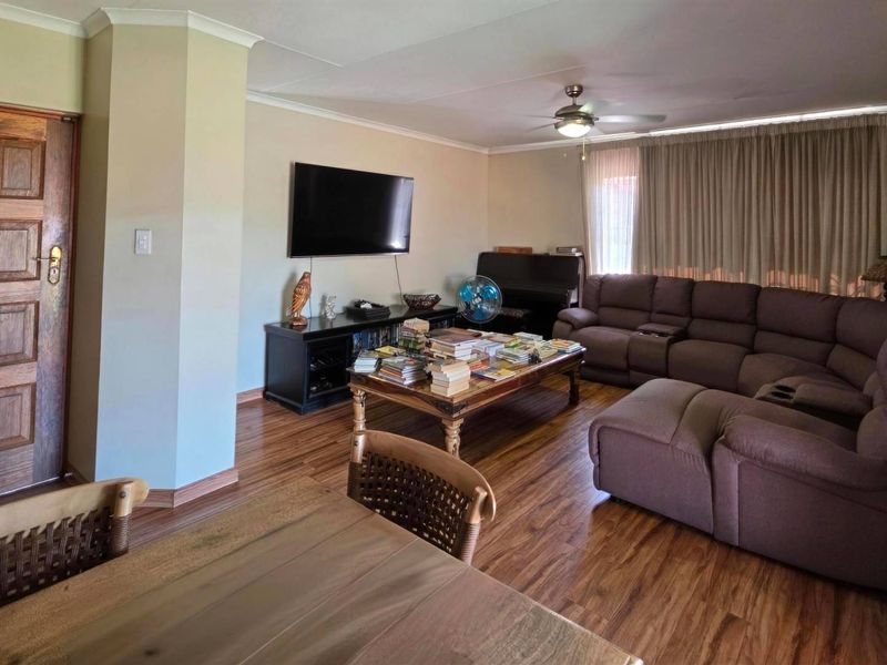 A spacious living room featuring laminate flooring, a ceiling fan, and classic cove cornicing, providing a comfortable and functional family living space.
