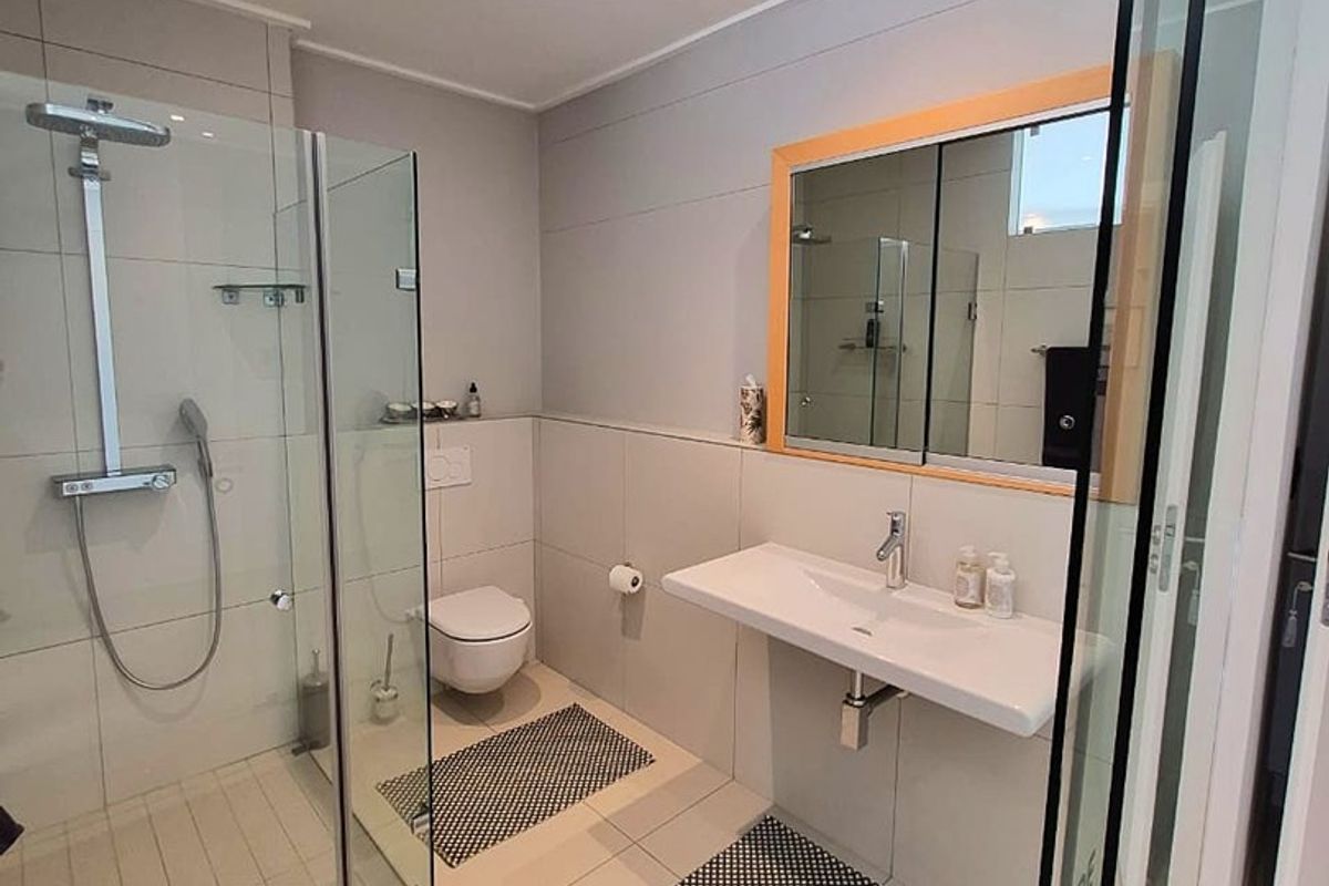 Modern bathroom featuring a walk-in glass shower, wall-mounted toilet, and a sleek wall-hung vanity basin with neutral tiling throughout.