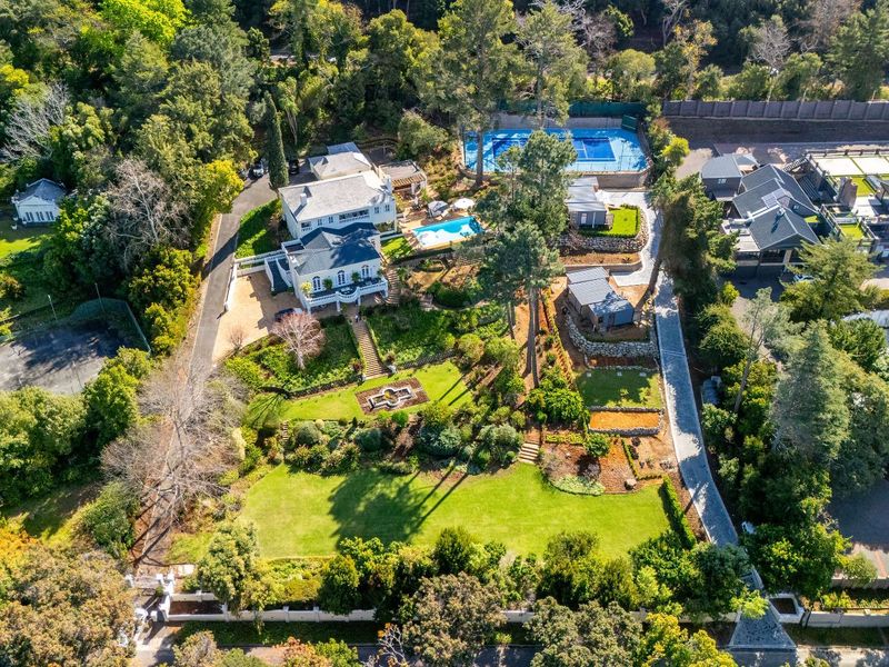 Aerial view of a large, well-maintained residential estate featuring extensive landscaped gardens, a swimming pool, and a private tennis court.