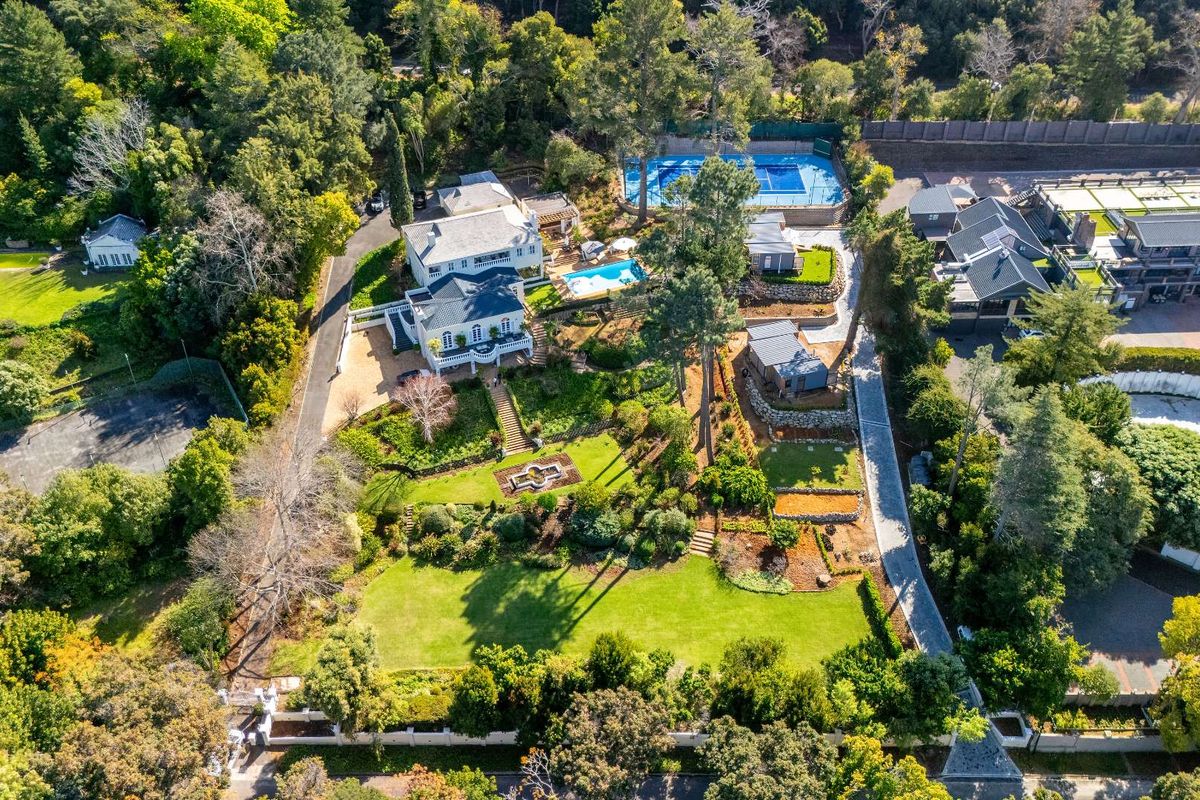 Aerial view of a large, well-maintained residential estate featuring extensive landscaped gardens, a swimming pool, and a private tennis court.