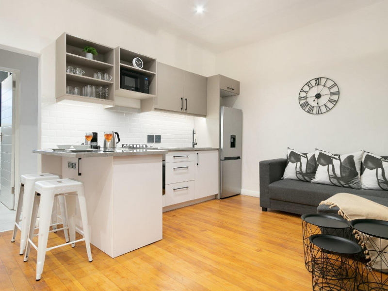 Modern open-plan kitchen and living area featuring sleek cabinetry, subway tile backsplash, and warm hardwood flooring.