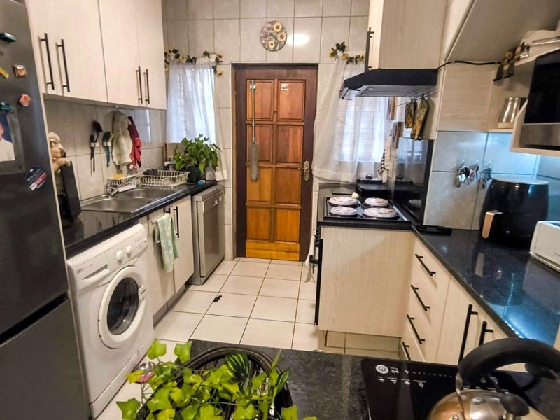 Functional galley-style kitchen featuring granite countertops, ample cabinetry, tiled backsplash, and integrated appliances, providing a practical workspace for daily cooking and laundry needs.
