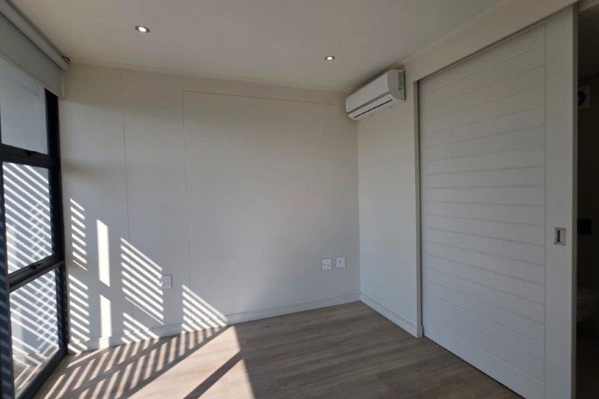 A bright, modern bedroom featuring laminate flooring, recessed lighting, a split-system air conditioner, and a sliding door leading to an adjoining space.