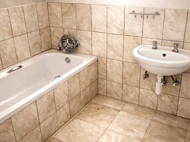 A functional bathroom featuring a bathtub and wall-mounted basin with neutral tiled finishes throughout.