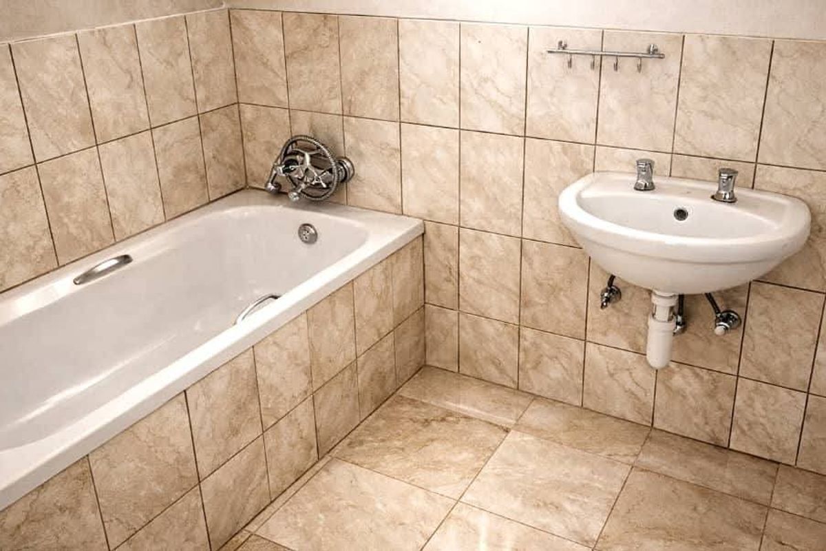 A functional bathroom featuring a bathtub and wall-mounted basin with neutral tiled finishes throughout.
