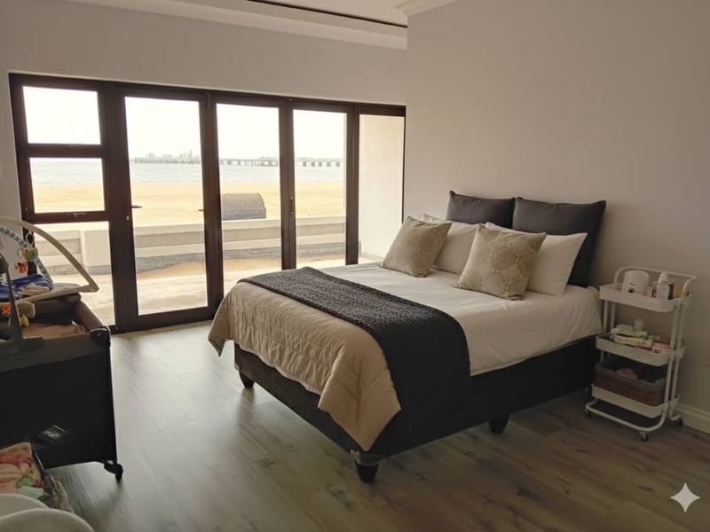 A bright bedroom featuring modern laminate flooring and large sliding glass doors that offer expansive views of the beach and ocean.