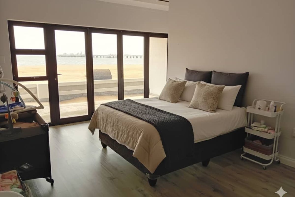 A bright bedroom featuring modern laminate flooring and large sliding glass doors that offer expansive views of the beach and ocean.