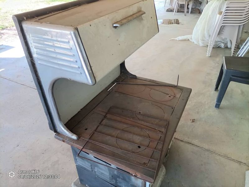 A vintage wood-burning stove located on a covered patio area, showing significant signs of age and surface corrosion.