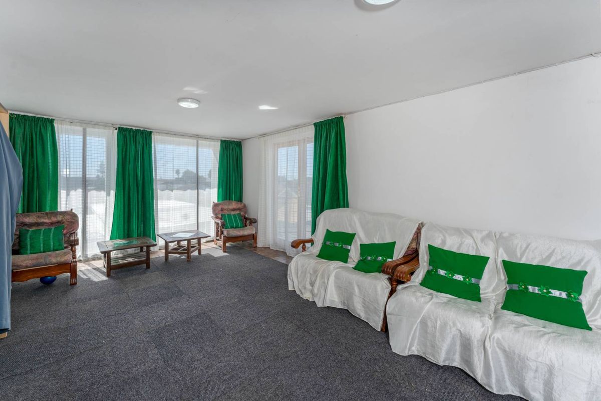 A spacious living room featuring large windows with natural light, carpeted flooring, and direct access to an outdoor area.
