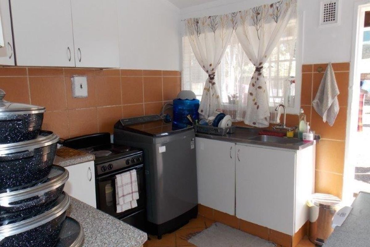 A functional kitchen featuring built-in cabinetry, a stainless steel sink, and tiled splashbacks, offering a practical layout with direct access to the exterior.