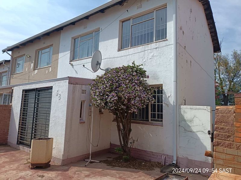 Front elevation of a two-story townhouse featuring white plastered walls with visible paint deterioration and security bars on windows.