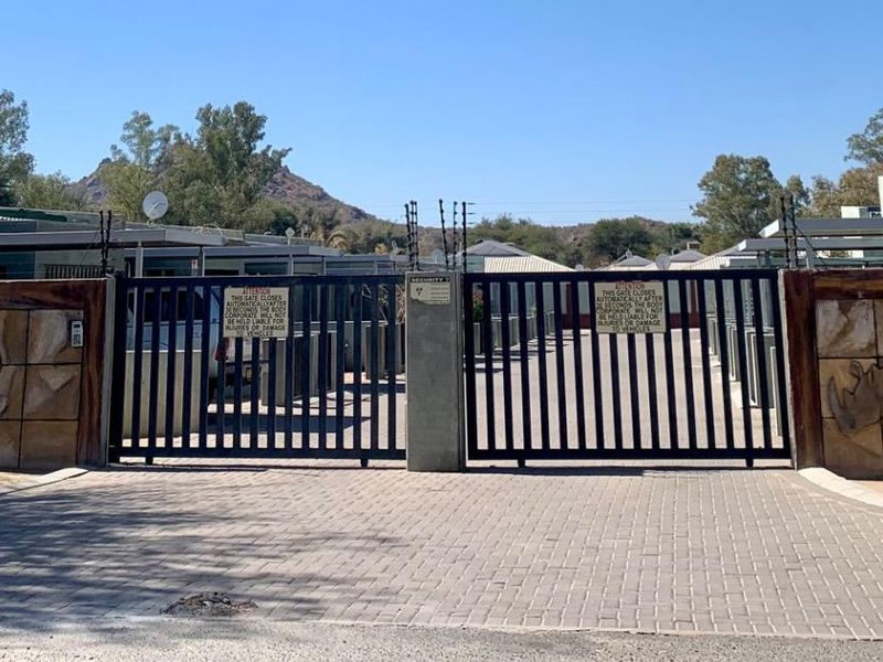 Secure gated entrance to the apartment complex featuring decorative stone relief walls, paved driveway, and perimeter electric fencing.